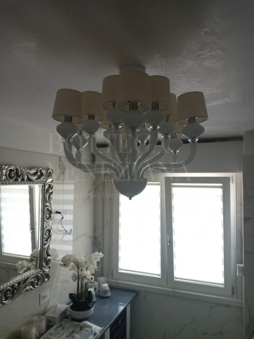 Raffinato lampadario moderno in vetro soffiato bianco decorato con paralumi bianchi. Fatto completamente a mano nella fornace di Bottega Veneziana a Venezia: ci troviamo nella terraferma veneziana a 10 minuti dall'aeroporto Marco Polo, raggiungibili in automobile. Prodotto secondo le tradizionali tecniche del vetro soffiato veneziano